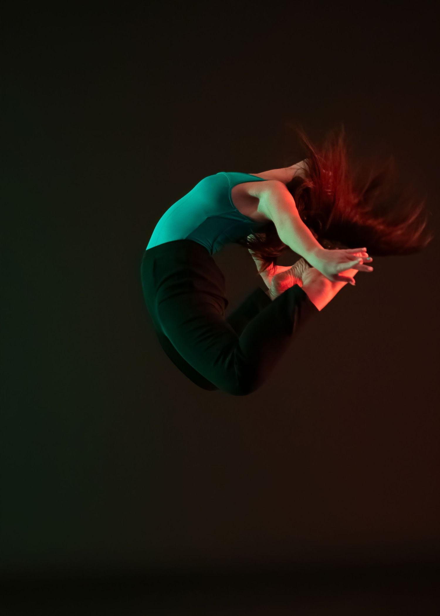 Dramatic sequence of a dancer in teal lighting performing a fluid motion against dark background.