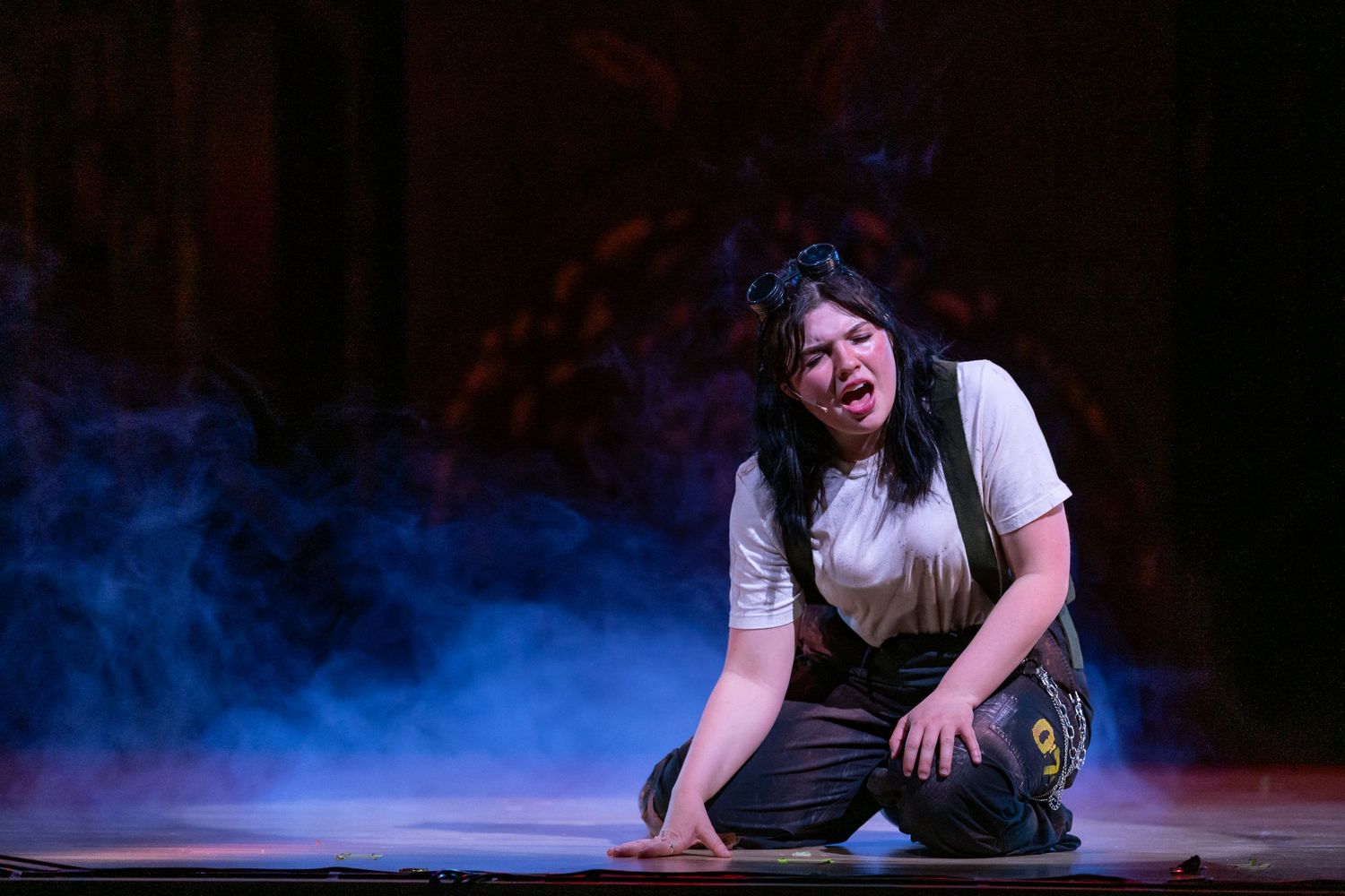 Theater performers in dark costumes on dimly lit stage during emotional scene.