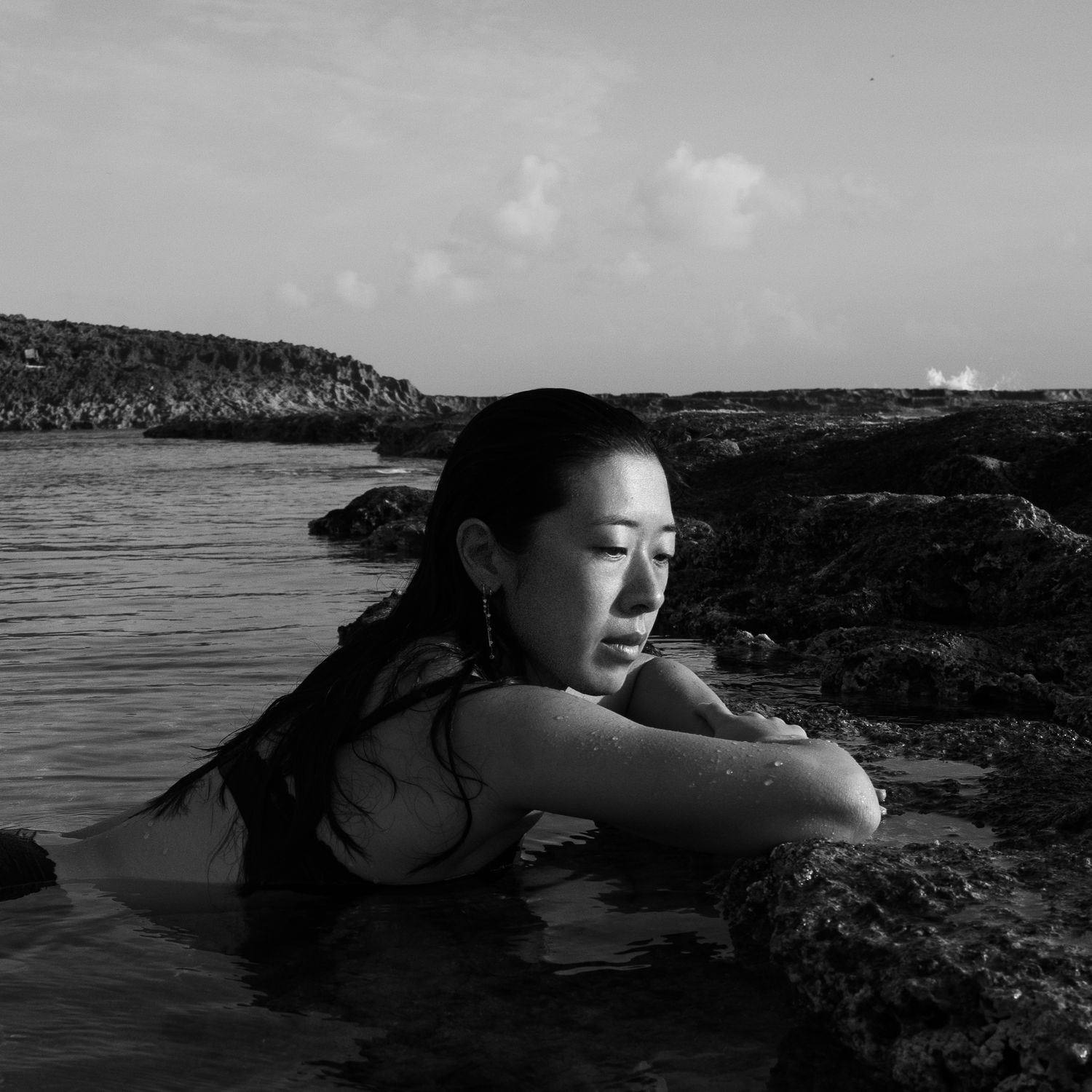 Black and white artistic photo series showing someone resting on coastal rocks by the ocean.