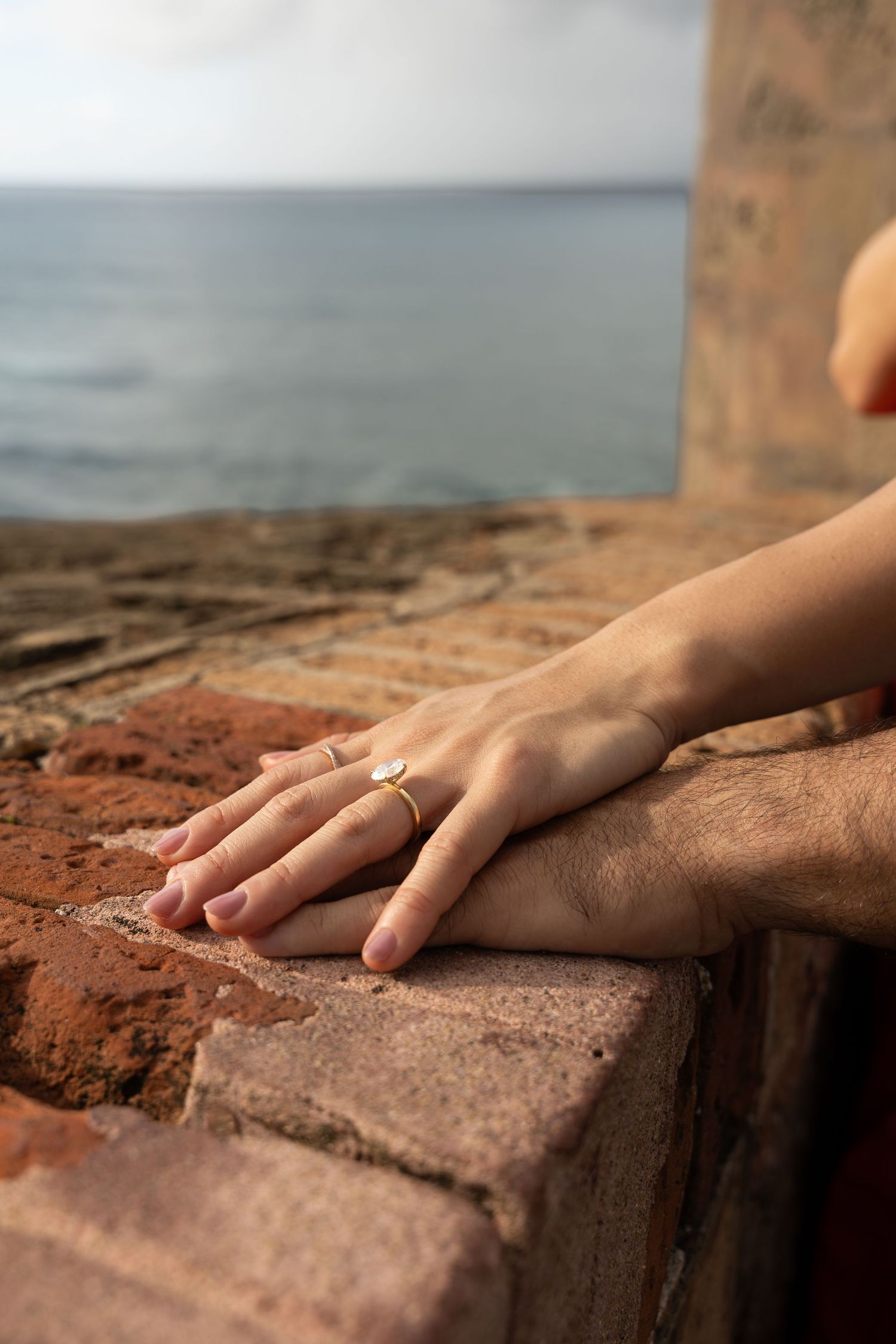 Close-up shots of hands with an engagement ring resting on weathered red stone.