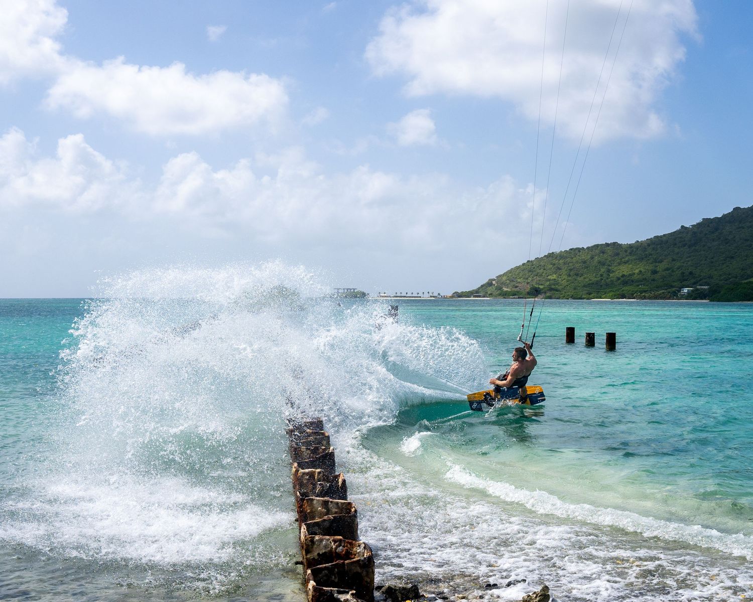 Kitesurfer creating dramatic splash while riding waves in crystal clear turquoise waters.