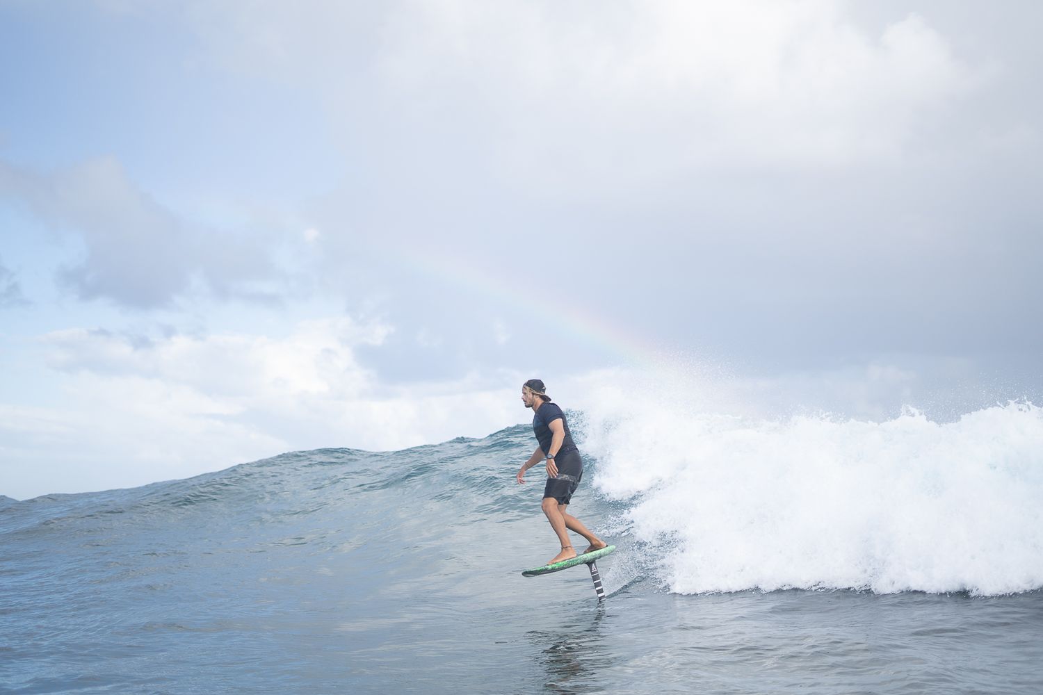 A surfer rides a large ocean wave against a cloudy sky.