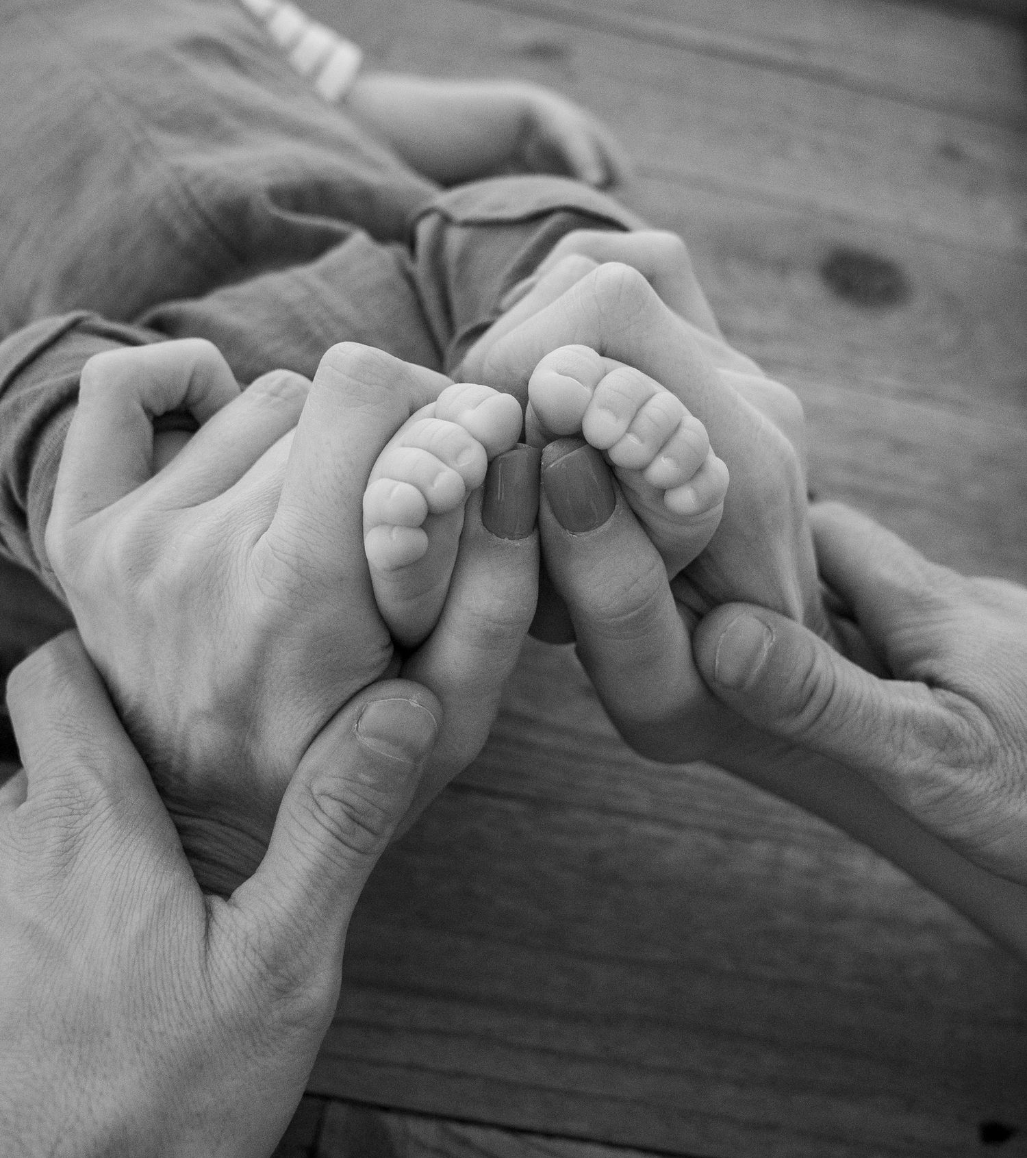 Black and white photo of two parents gently holding their newborn baby's tiny feet in their hands.