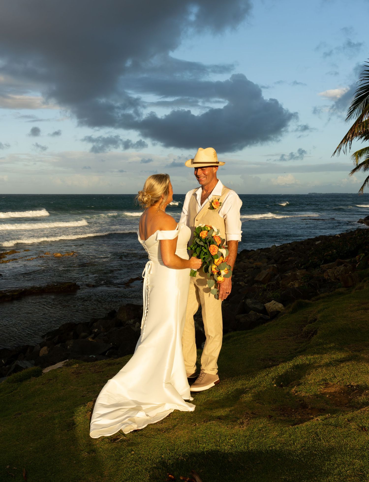 A couple shares an intimate moment during their beach wedding ceremony at sunset with dramatic clouds overhead.