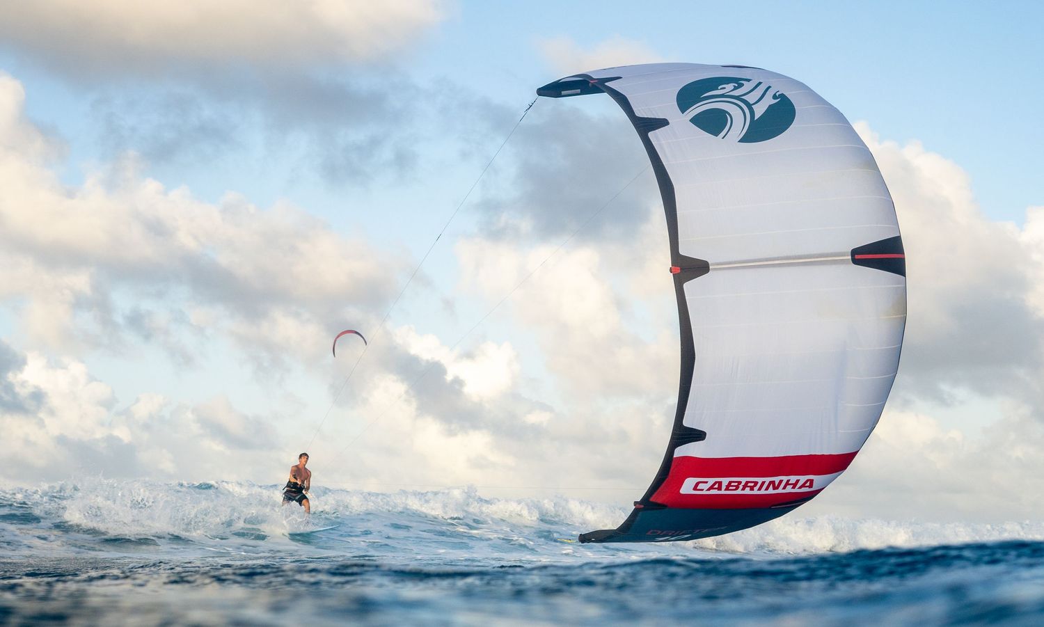 kiteboarder catching waves against cloudy sky over blue ocean.