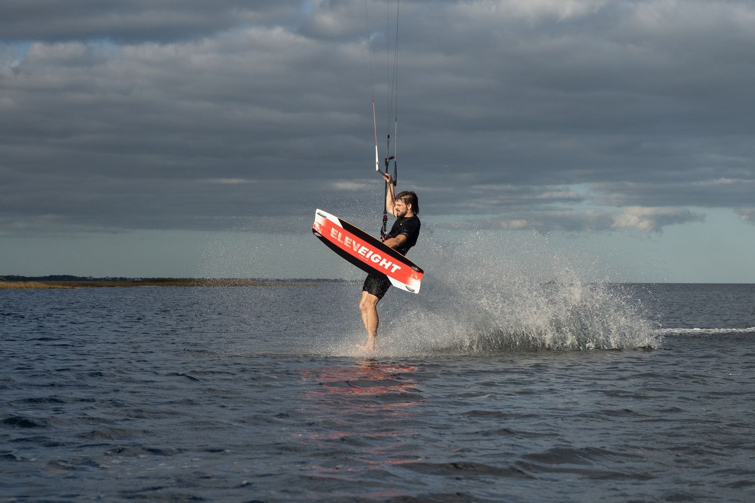 Kitesurfer performing a dynamic jump maneuver over choppy waters against a dramatic cloudy sky.