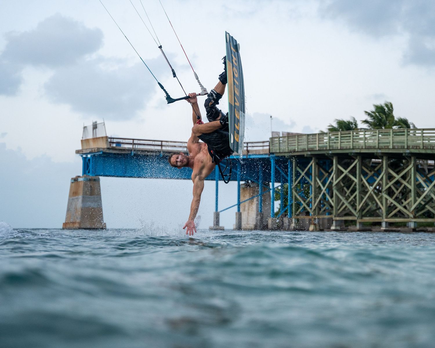Low angle water view of kitesurfing action near a pier structure.