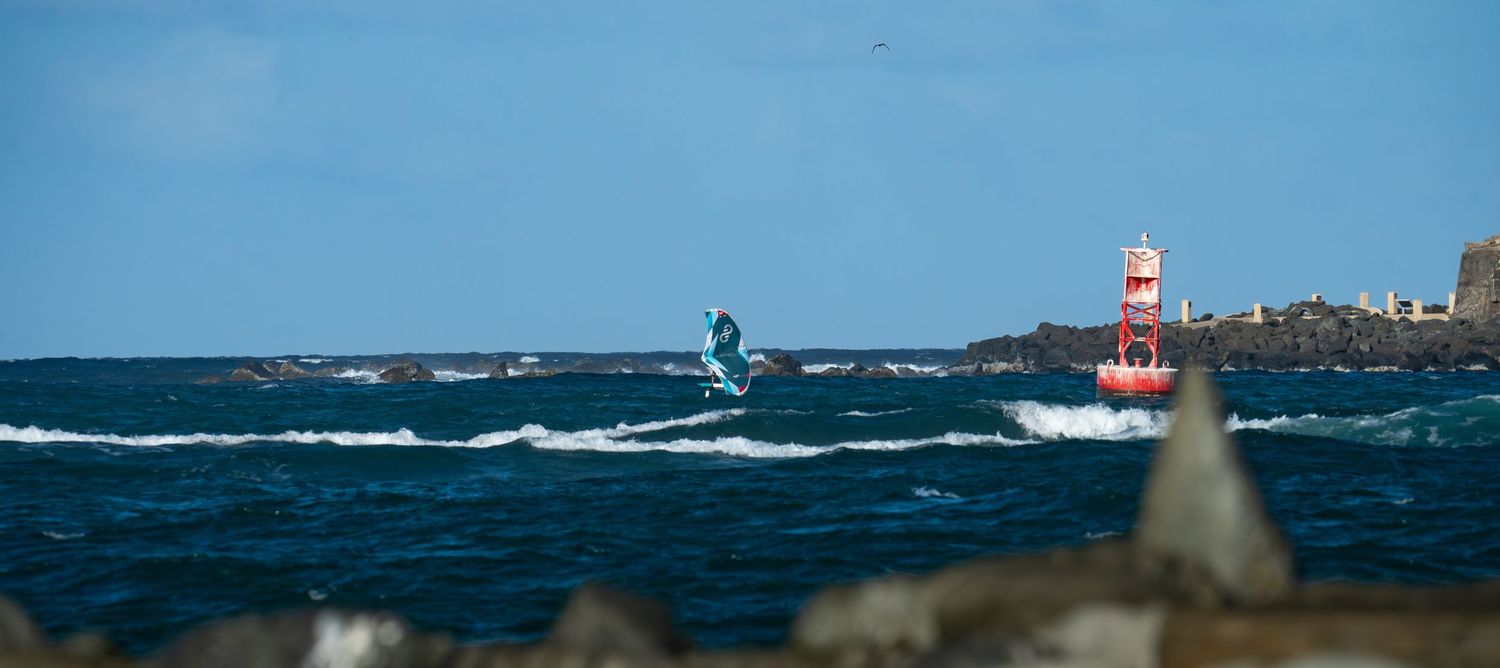 Kitesurfer jumping near a red and white lighthouse on a windy ocean day.