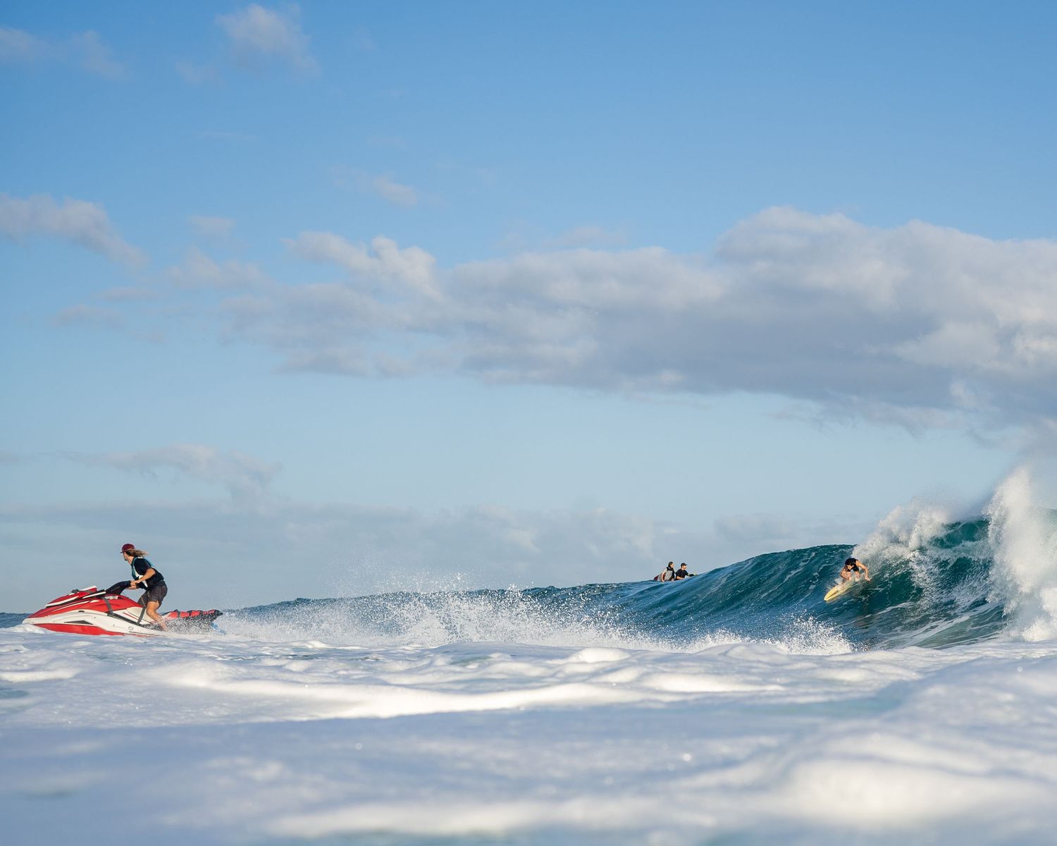Jet ski rider navigating through large ocean waves with breaking surf in the background.