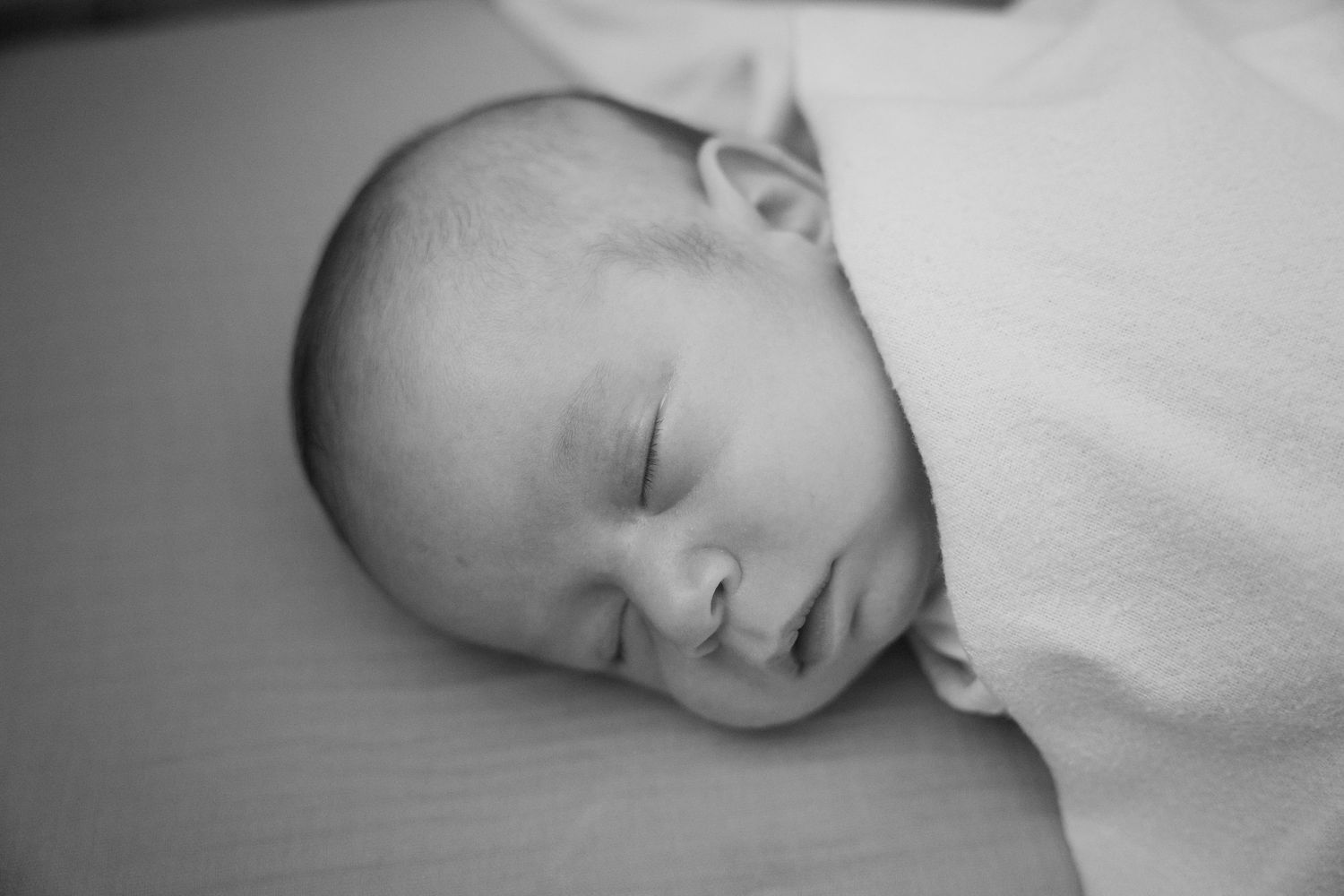 Black and white photo of a peaceful sleeping newborn baby wrapped in a soft white blanket.