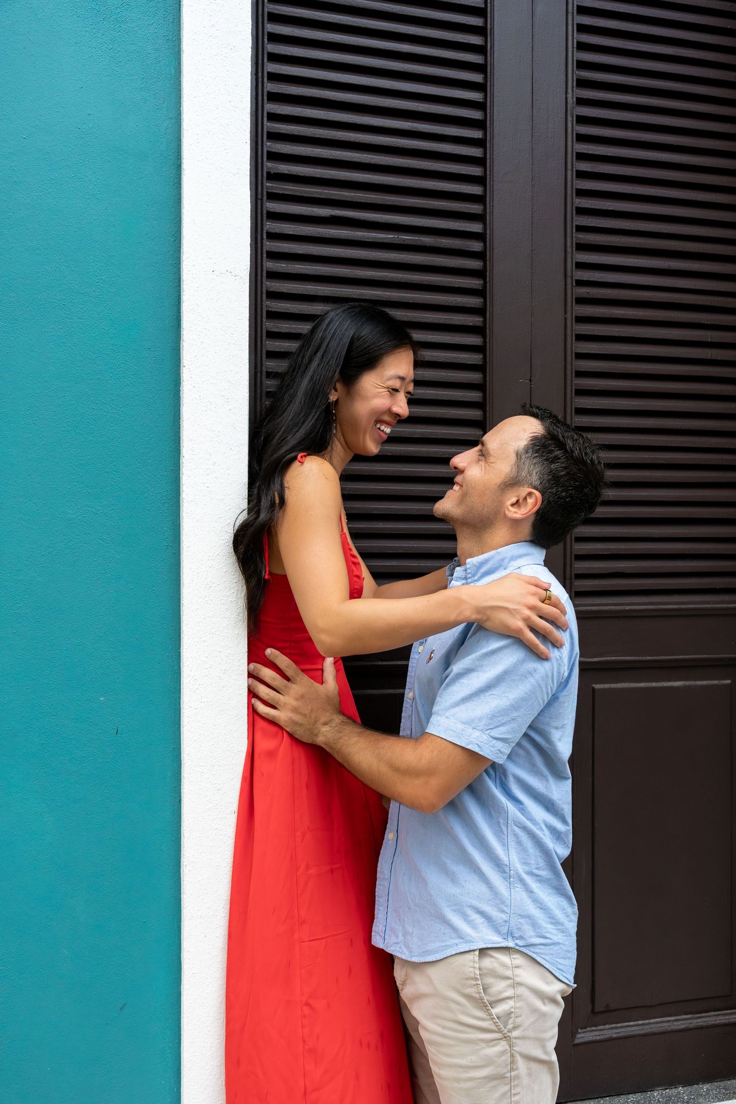 A playful couple's photoshoot against a turquoise wall with black shutters.