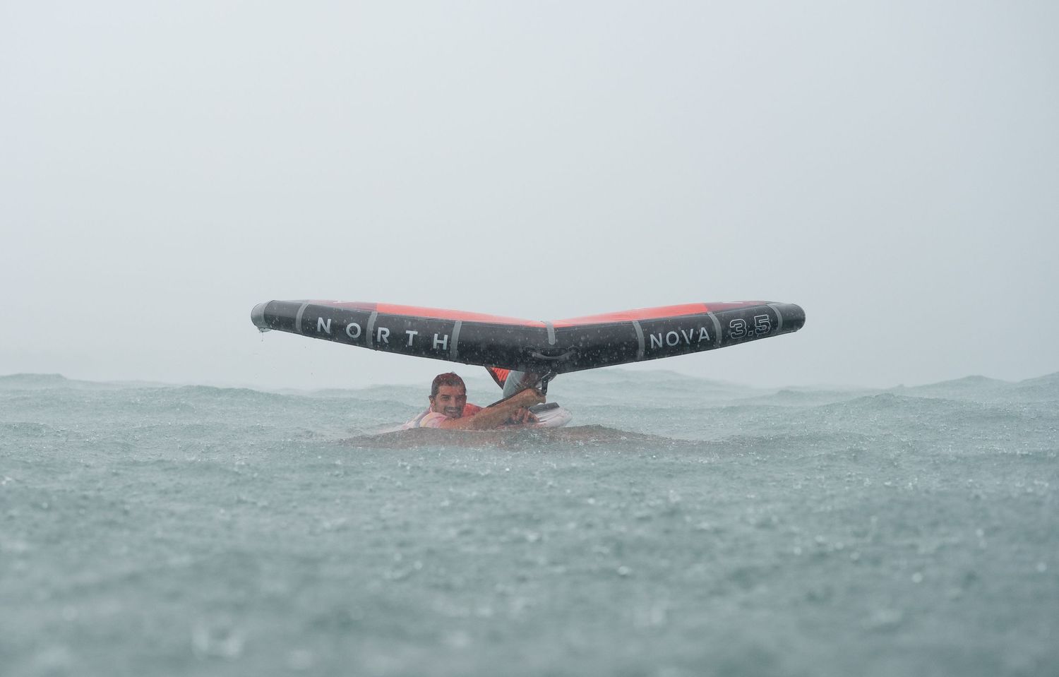 Kiteboarding wing emerging from rough ocean waters during stormy conditions.
