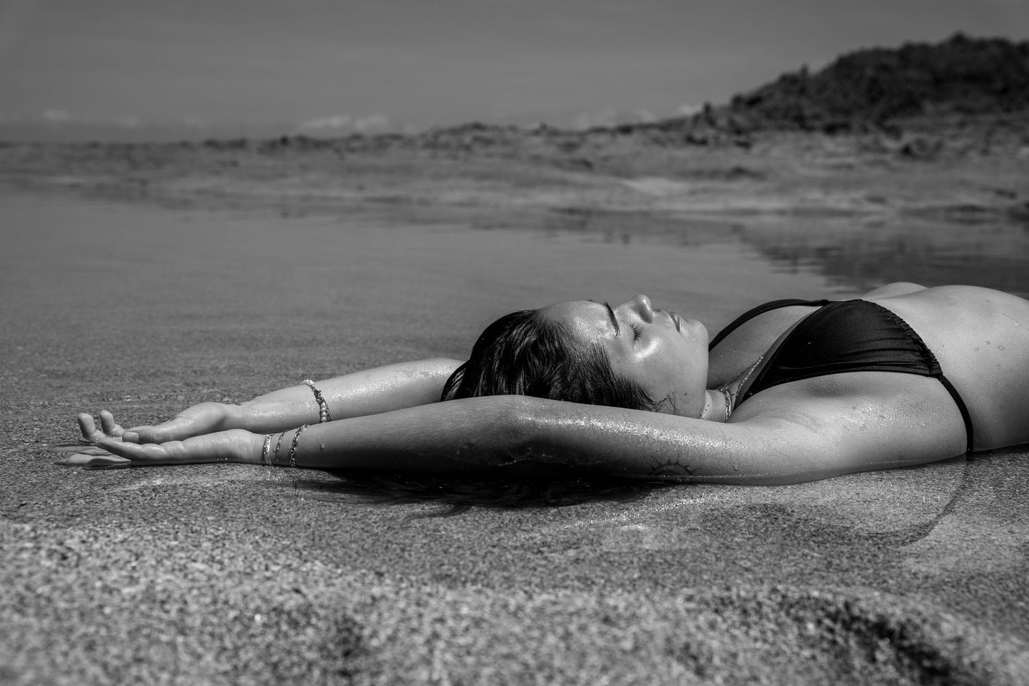 Minimalist black and white photos of person lying on beach with ocean waves in background.