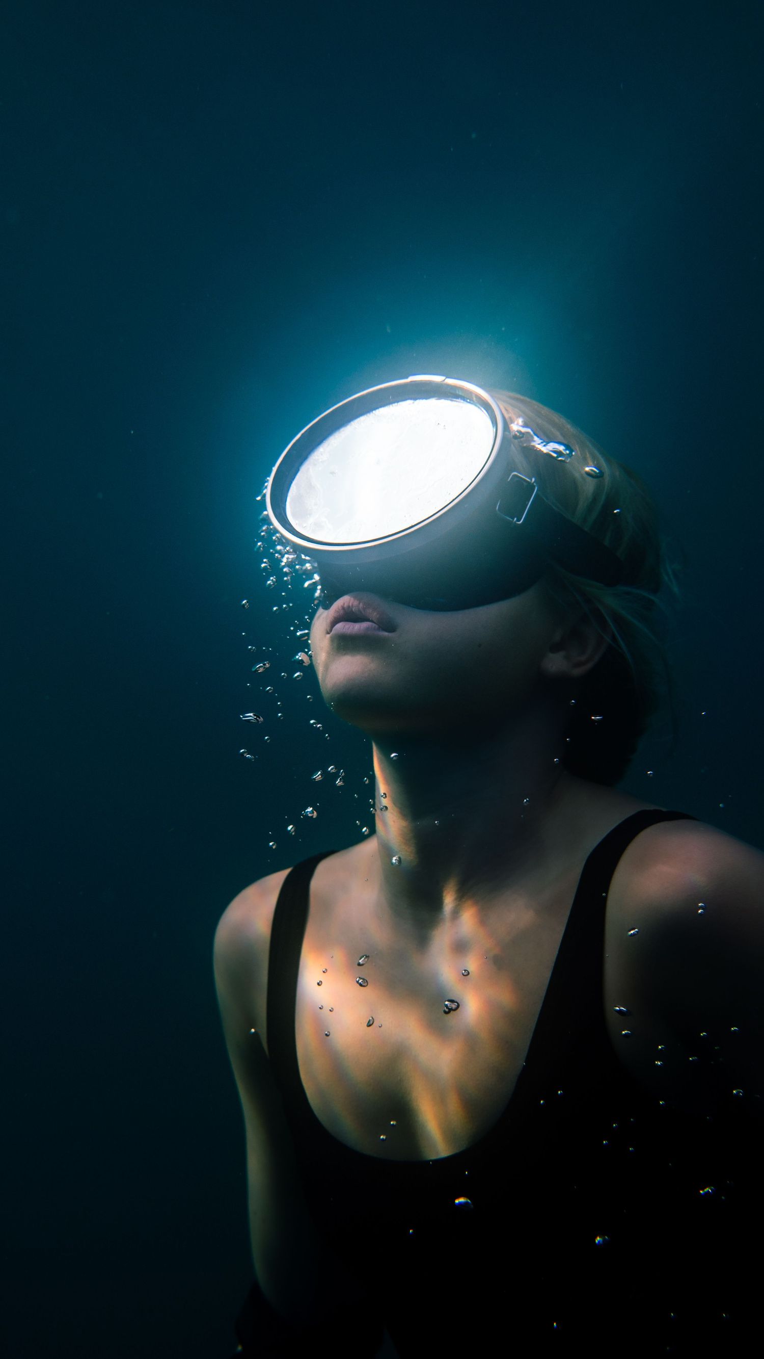 Artistic underwater portrait with virtual reality headset glowing in dark blue waters.