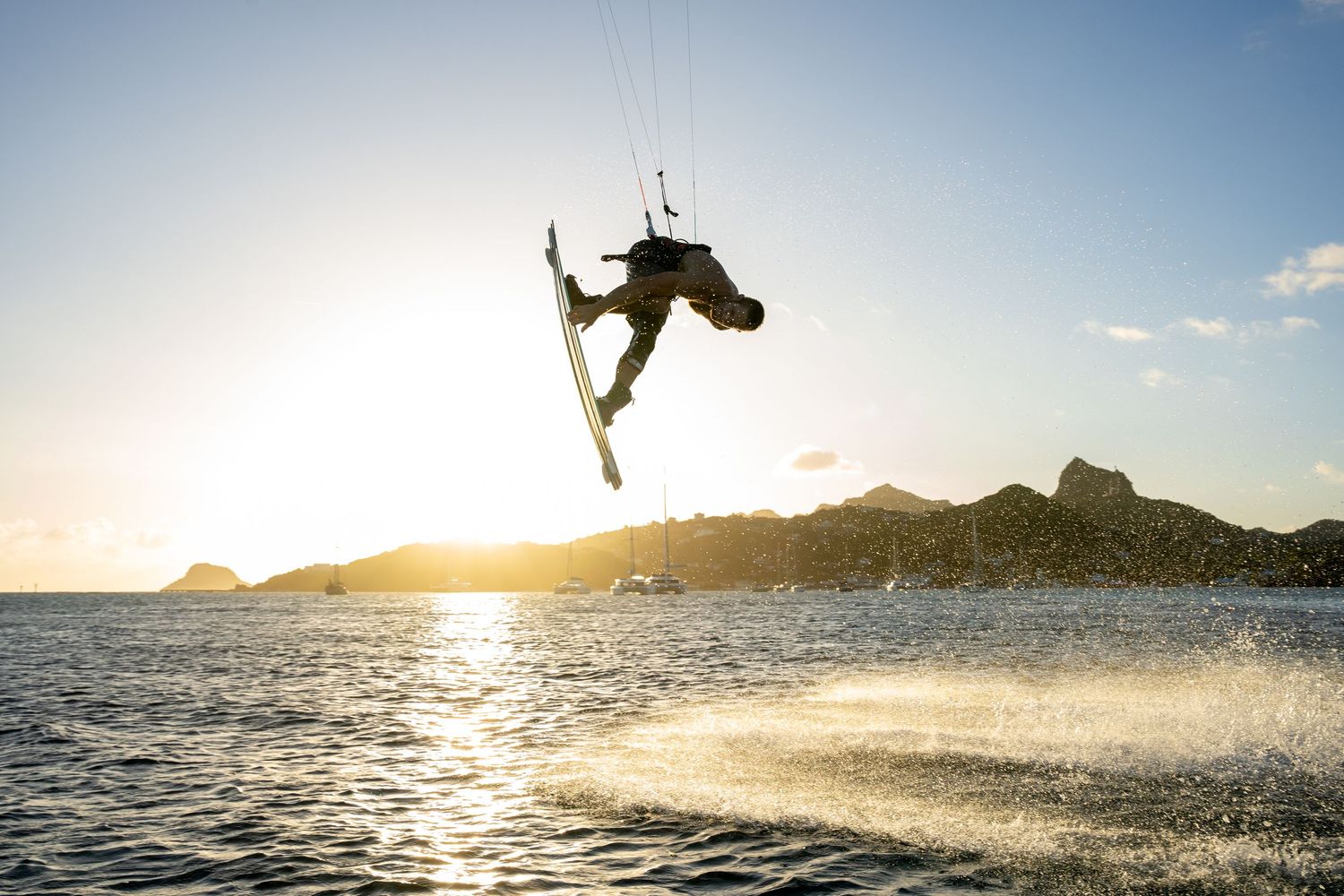Kitesurfer performs aerial tricks against golden sunset sky over ocean.