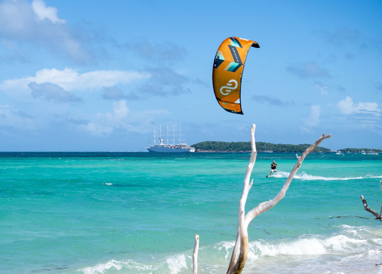 Colorful kites flying in bright blue sky over turquoise tropical waters.