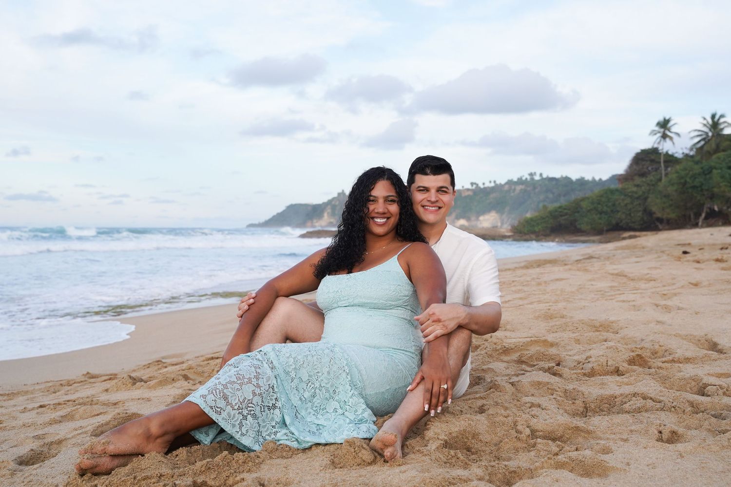 A couple enjoys a romantic photoshoot on a scenic beach with waves and palm trees in the background. Engagement photoshoot in puerto rico