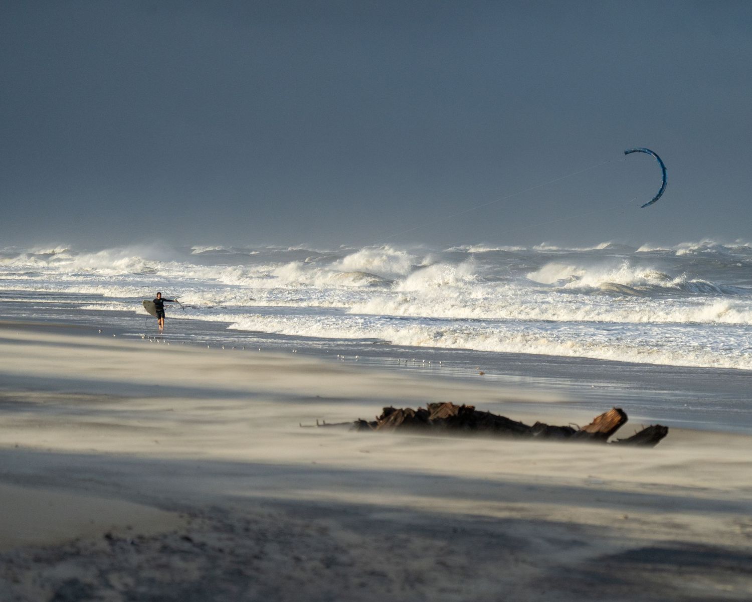 Silhouetted kitesurfer against dramatic cloudy sky at sunset on a beach.