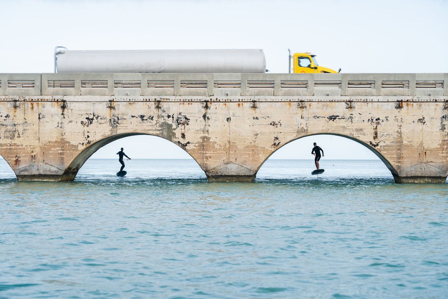 Wide panoramic view of efoilers near a concrete breakwater structure in blue waters.
