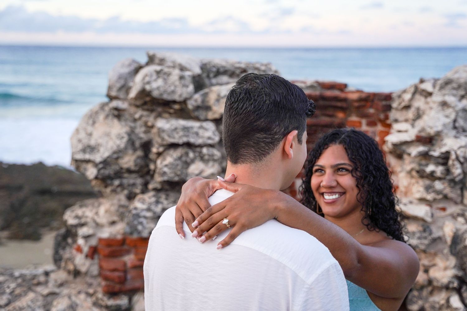 A romantic proposal sequence on a rocky beach with crashing waves in the background.