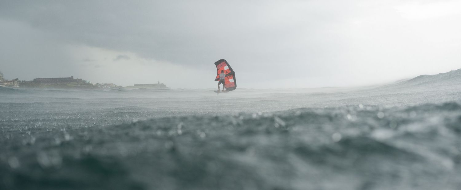 Red kite visible in distance over choppy ocean waters on an overcast day.