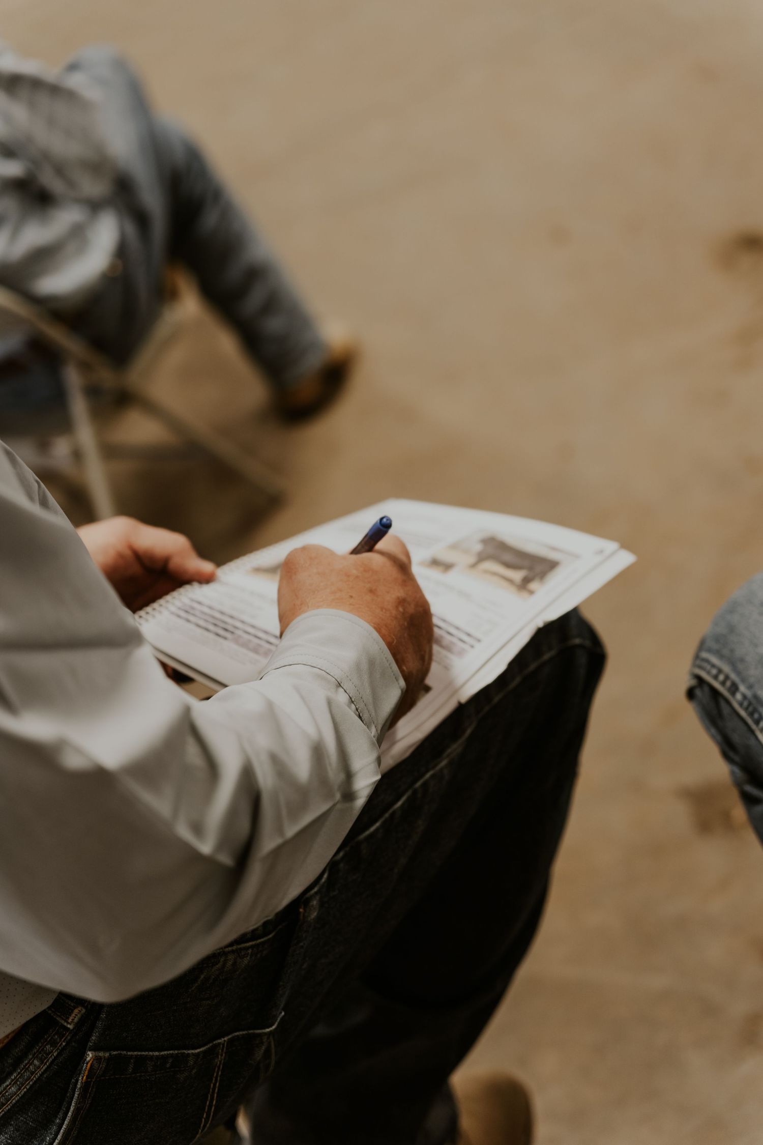 Person writing on a document with a blue pen while seated, viewed from above in an outdoor setting.