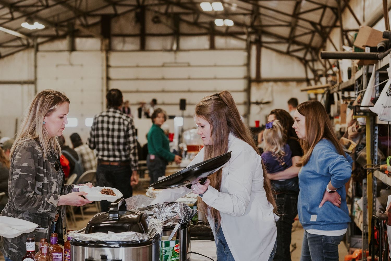 Women browsing and shopping at an indoor flea market or craft fair inside a rustic warehouse venue.