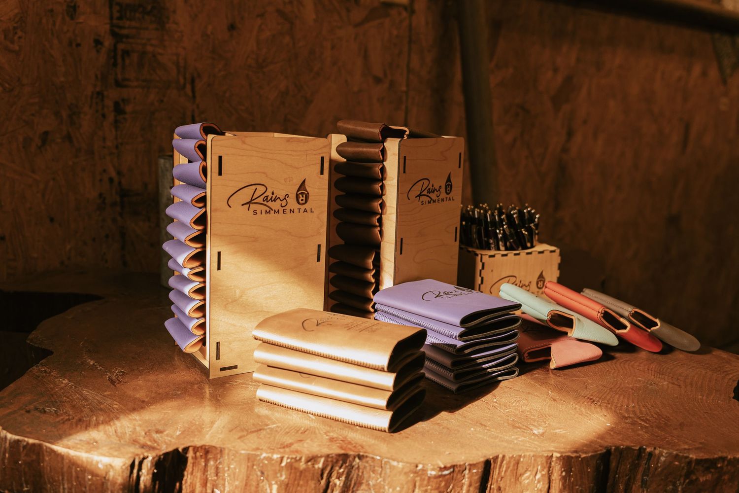 Rustic wooden gift boxes with branded notebooks and pens displayed on a wooden stump in warm lighting.