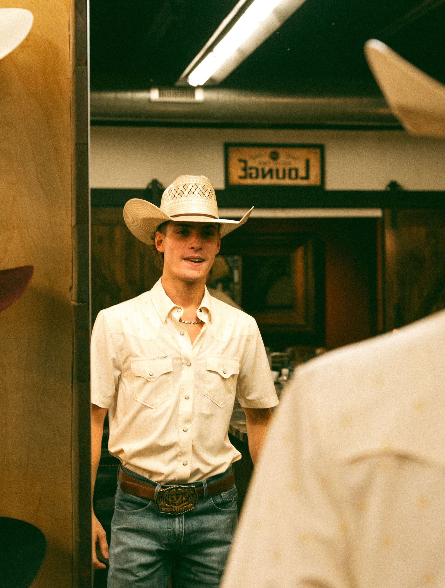 Young man in cowboy hat and jeans standing in a western store near a lounge sign.