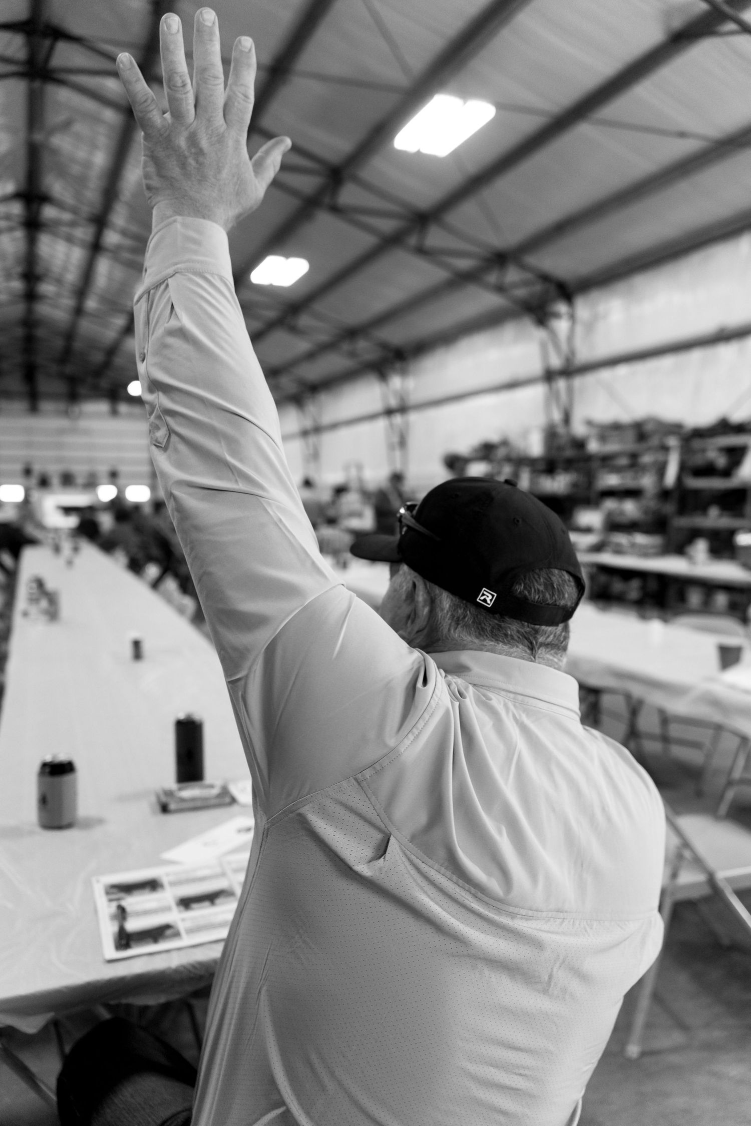 Black and white photo of a man in a cap raising his hand at an indoor auction event.