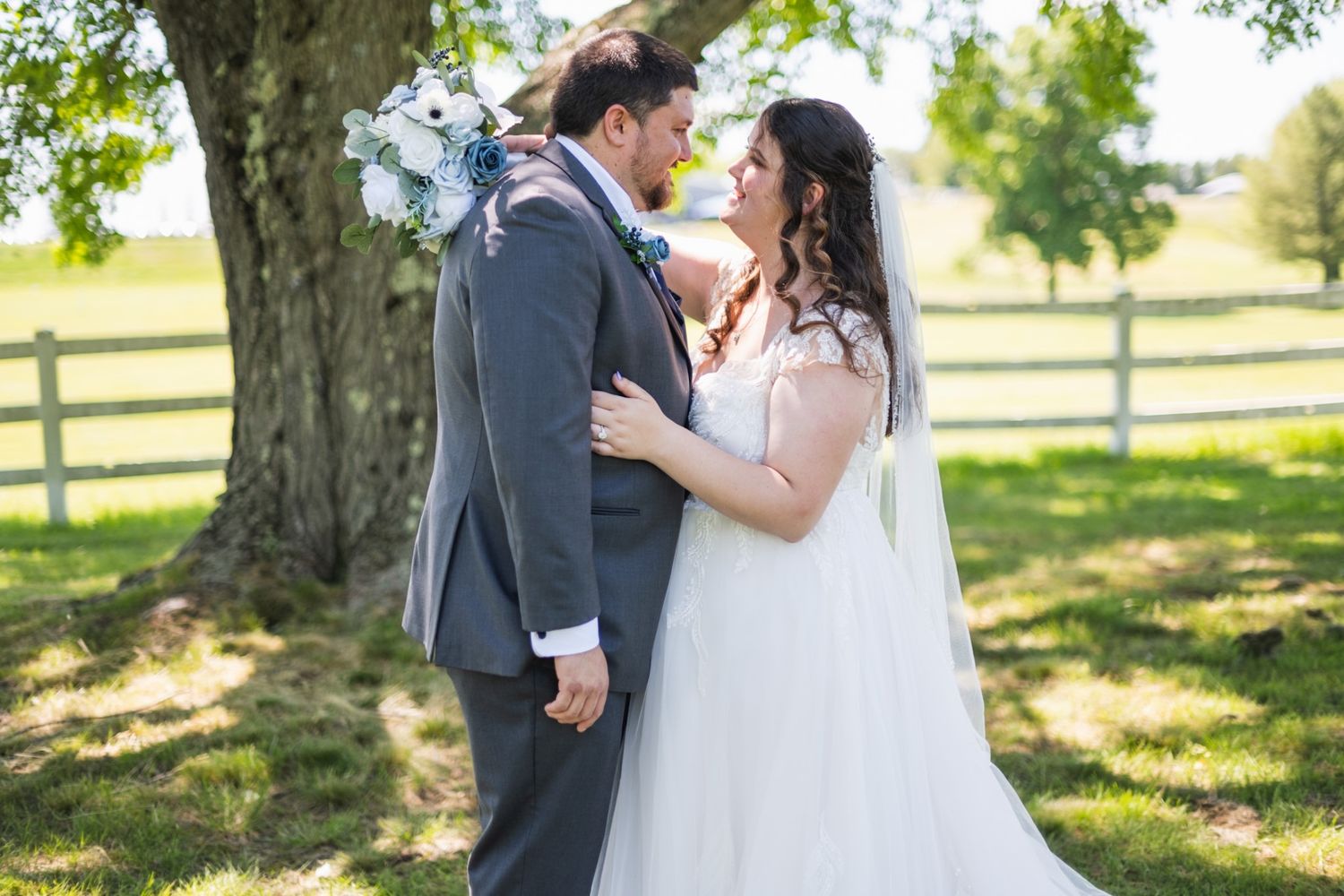 A couple shares an intimate moment during their outdoor wedding photoshoot under sunlit trees.