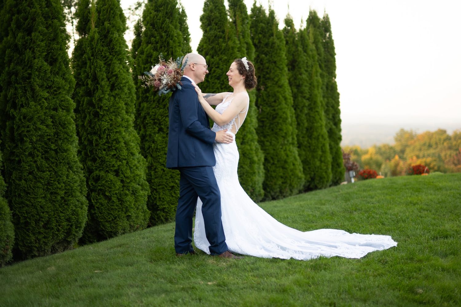 Wedding couple poses for romantic portraits among tall evergreen trees at sunset.