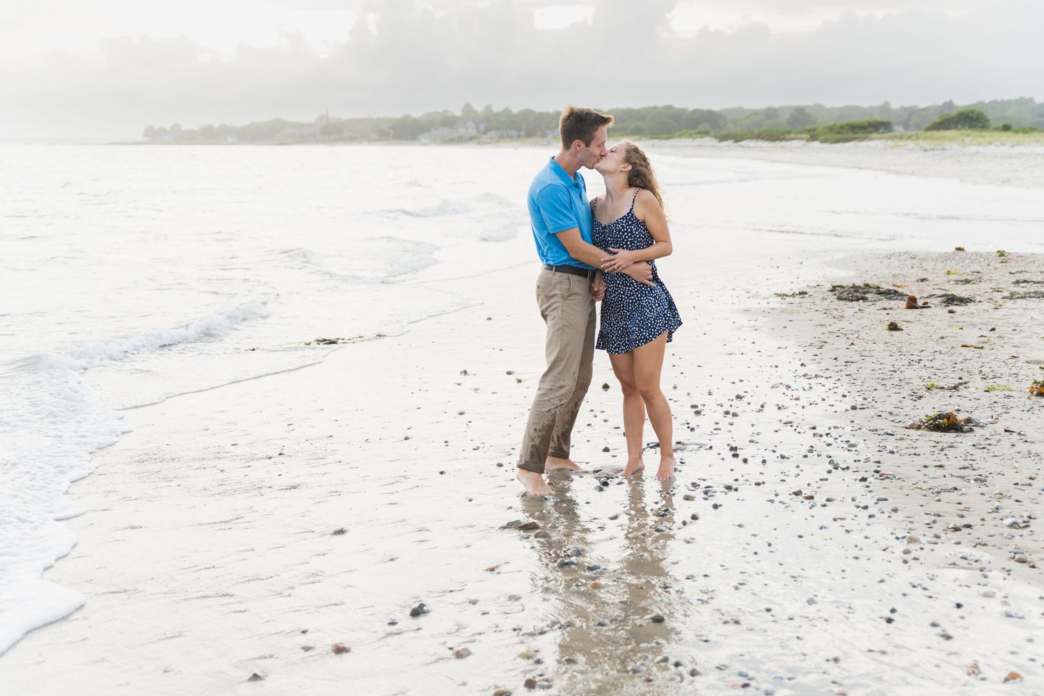 Couple standing together on a misty beach during sunset with waves washing up on the shore.