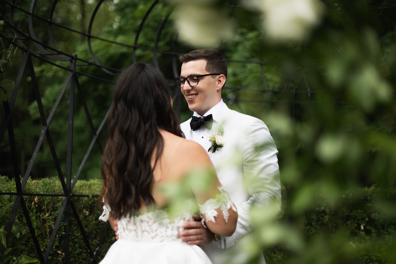 A romantic first look moment unfolds between newlyweds surrounded by lush garden foliage.