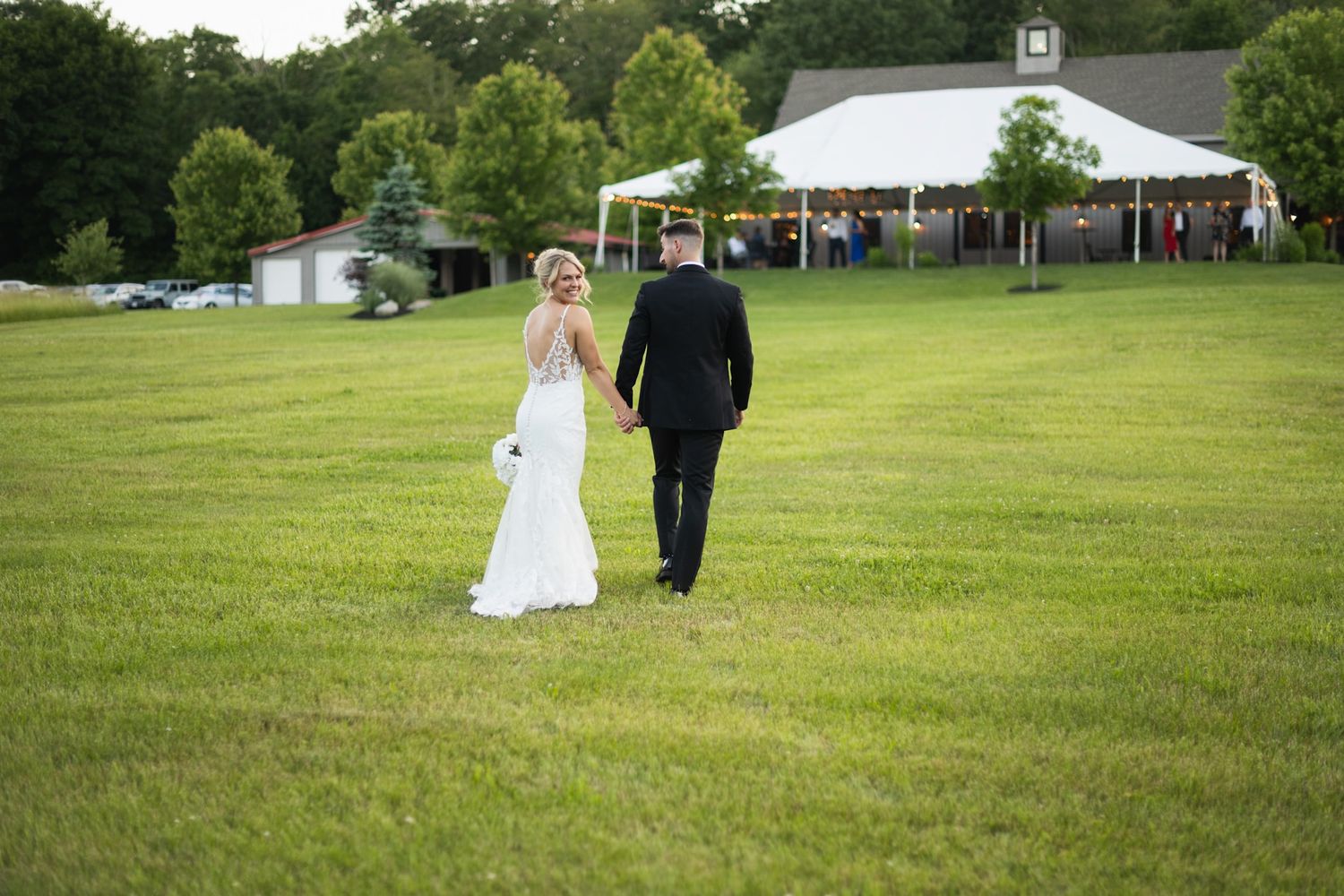 Couple walking together across a lush green field with trees in the background.