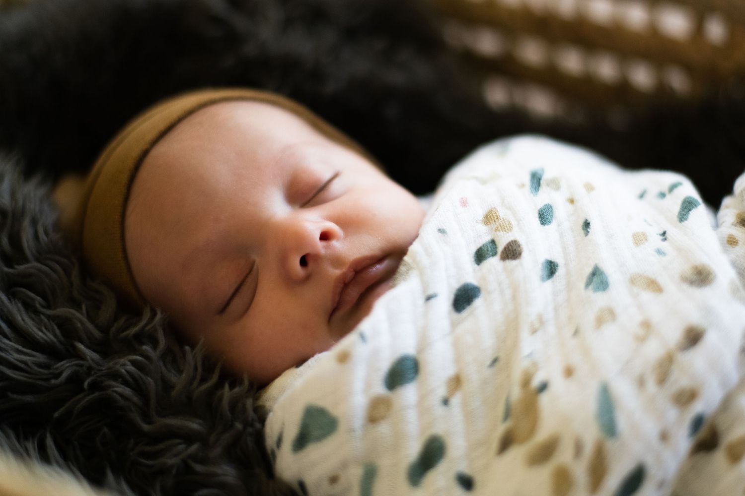 Peaceful newborn sleeping while wrapped in white patterned swaddle.