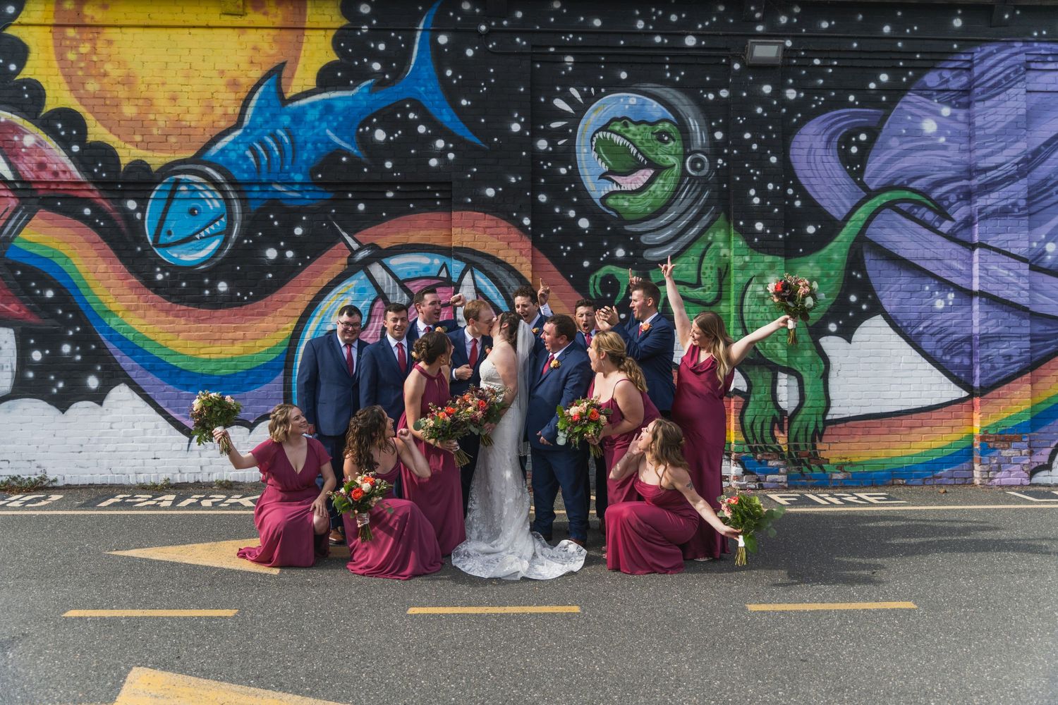 Wedding party poses against vibrant street art mural featuring cosmic designs and swirling colors.