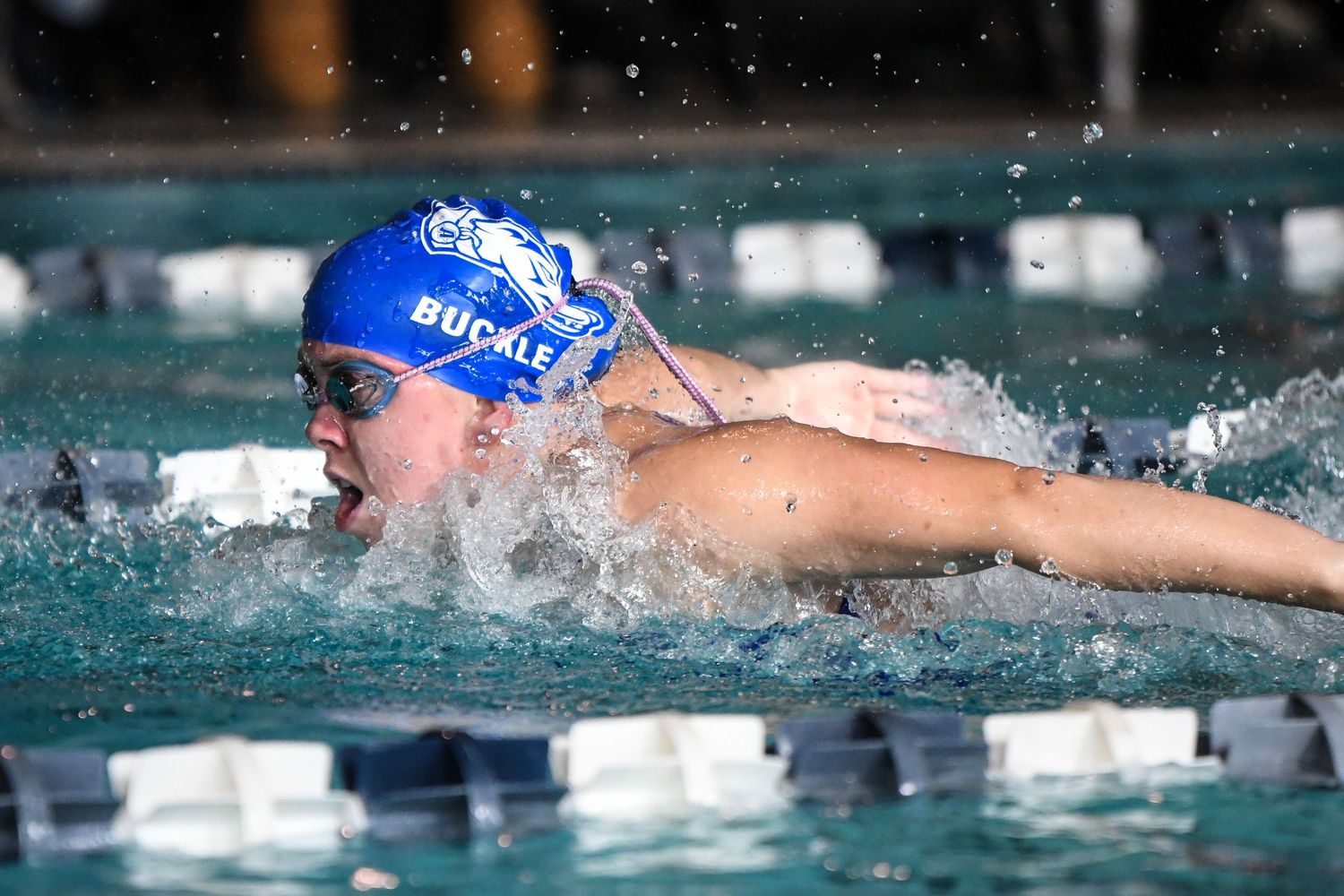 Swimmer Buckle competes in butterfly stroke during a competitive indoor swim meet.