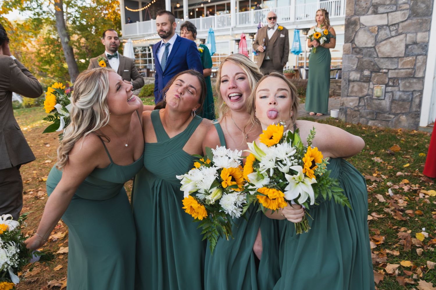 Bridesmaids in emerald green dresses hold sunflower bouquets outdoors.