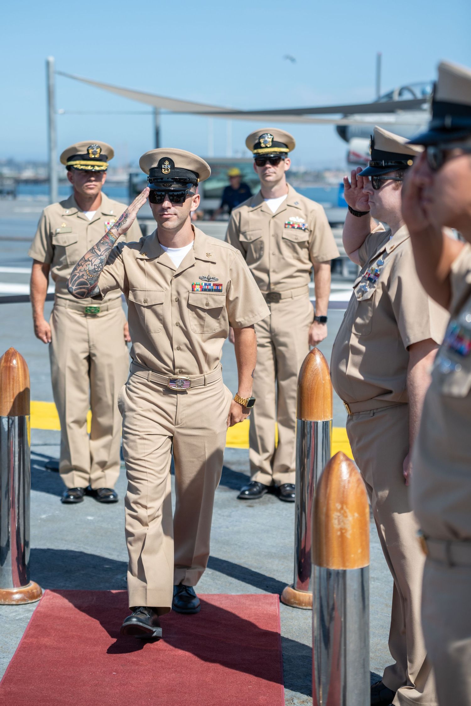 Naval officers in dress uniforms standing at attention on red carpet during military ceremony.