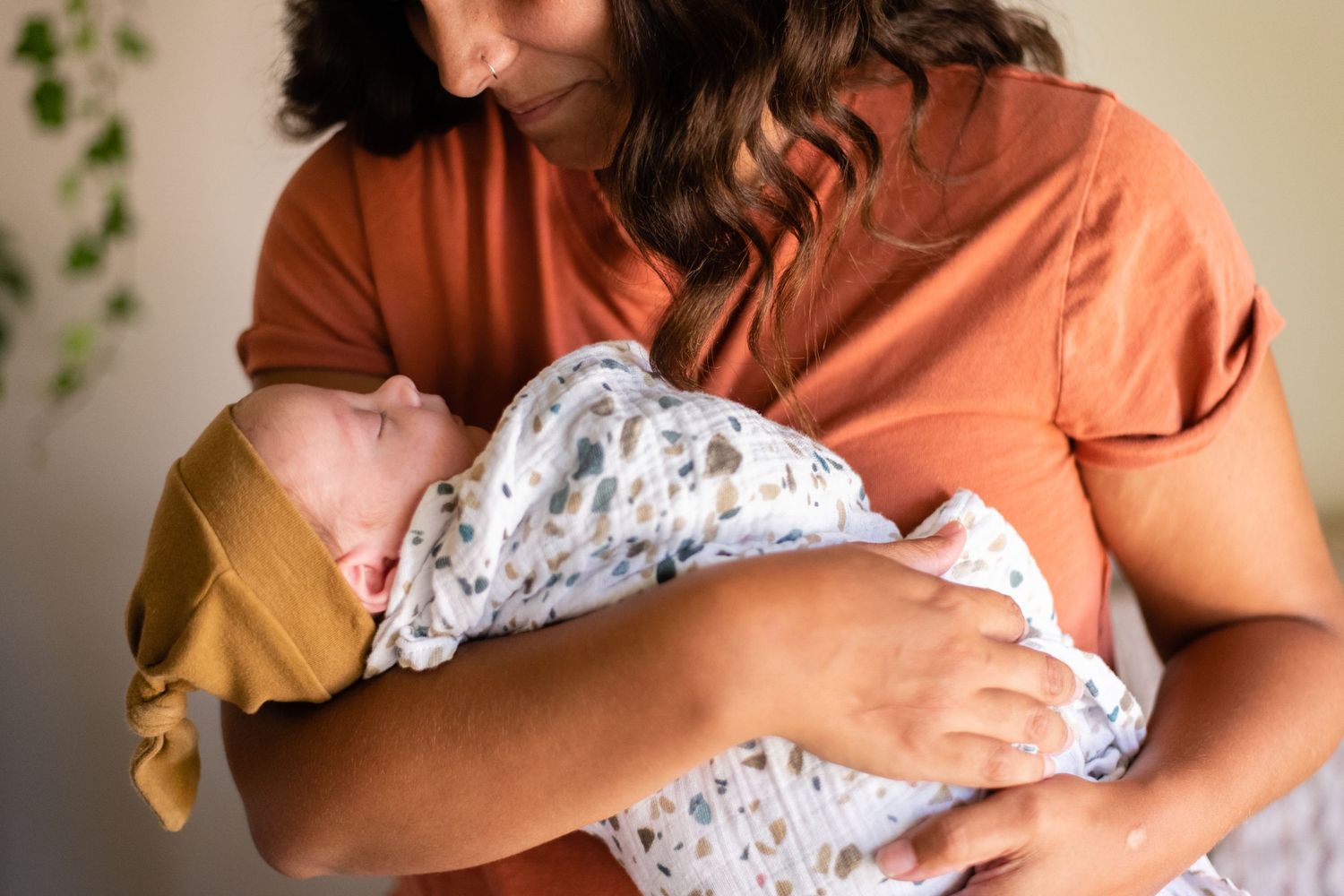 Intimate newborn photoshoot showing gentle moments with baby wrapped in patterned swaddle.