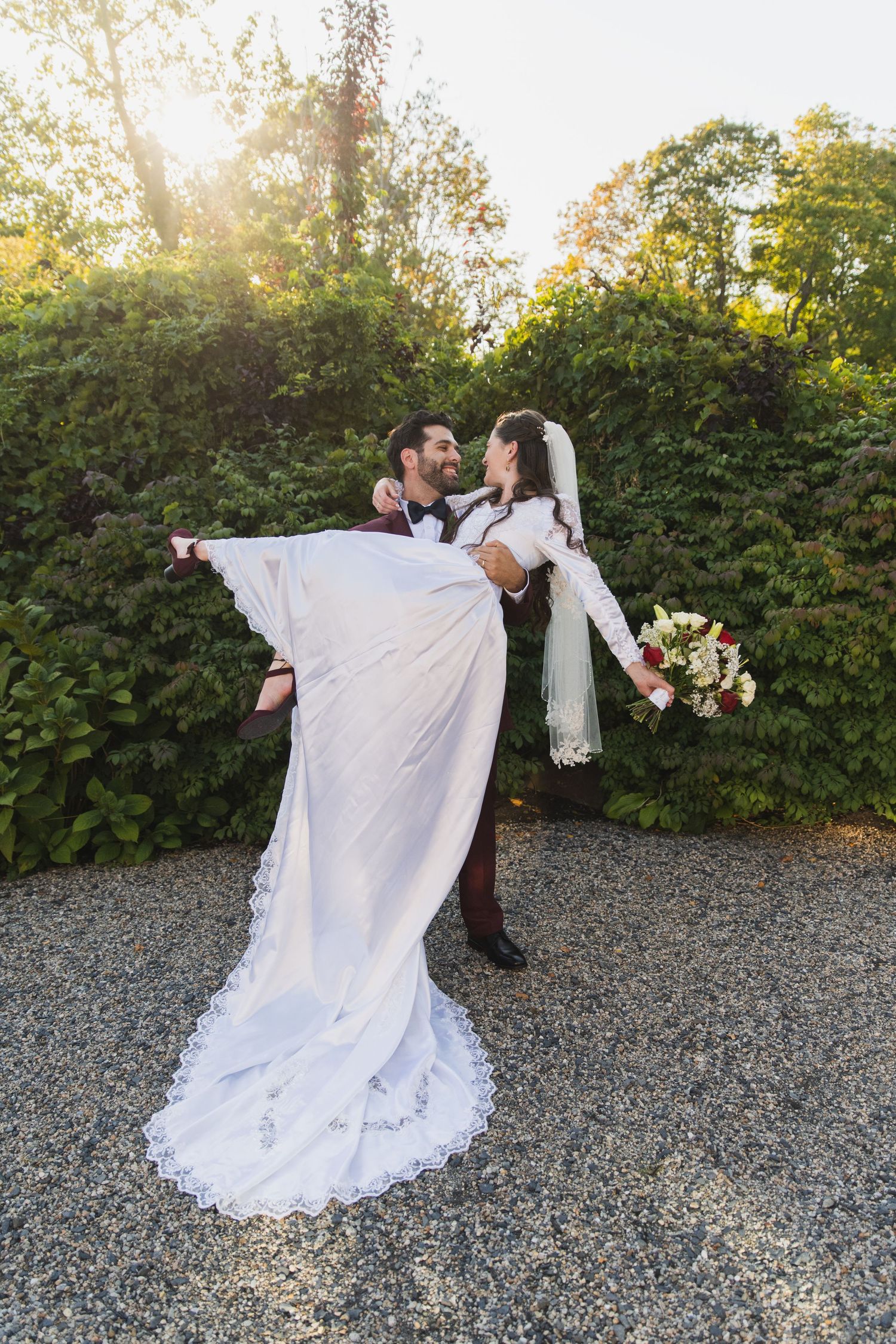A romantic wedding couple dancing and twirling outdoors with a white dress flowing in the autumn sunlight.