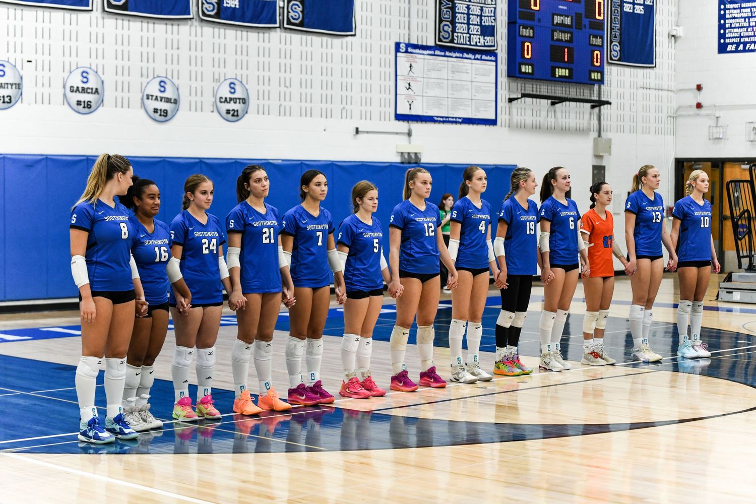 Girls volleyball team in blue uniforms lined up on indoor court before a match.