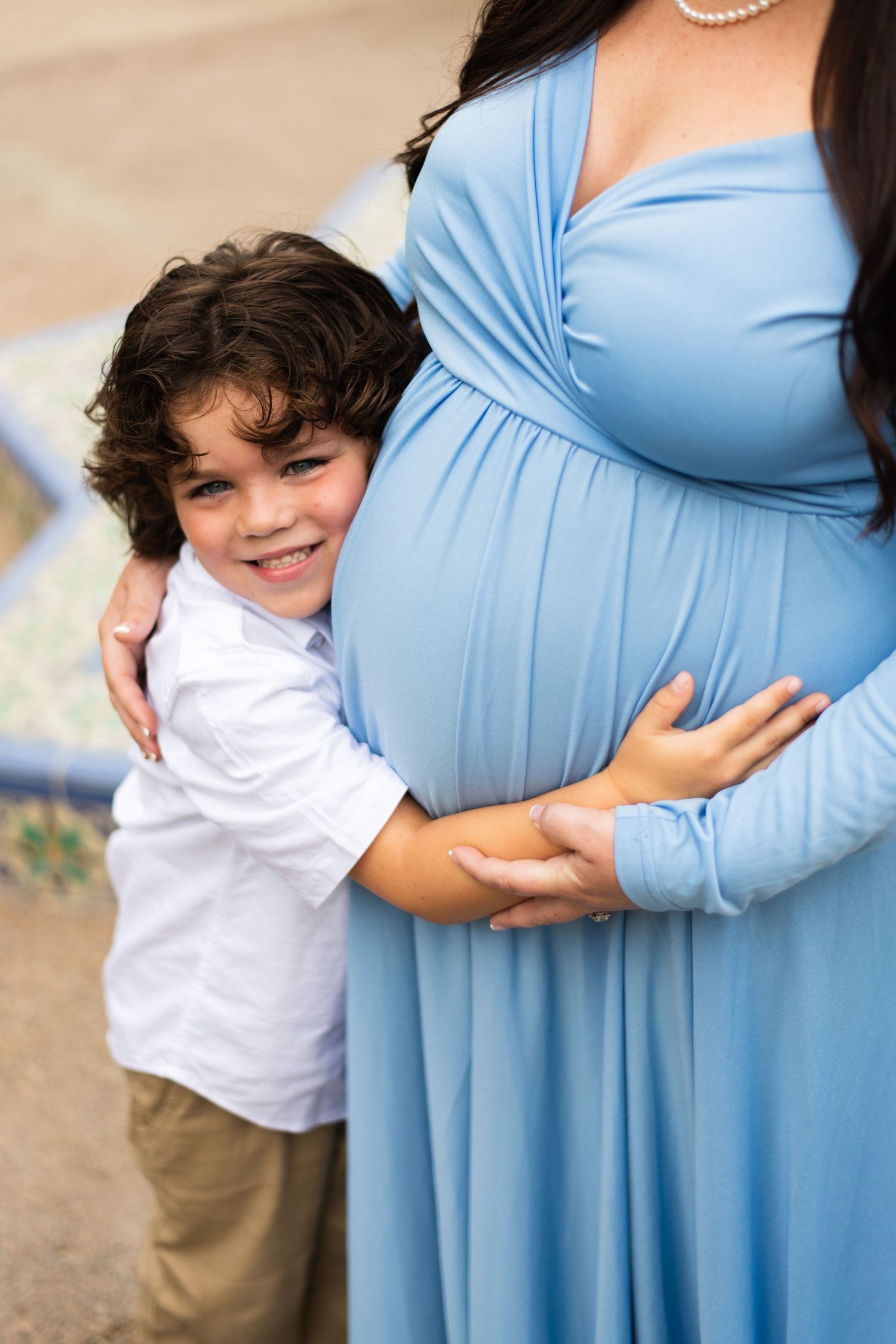 A heartwarming maternity photo showing embrace in soft blue dress against neutral background.