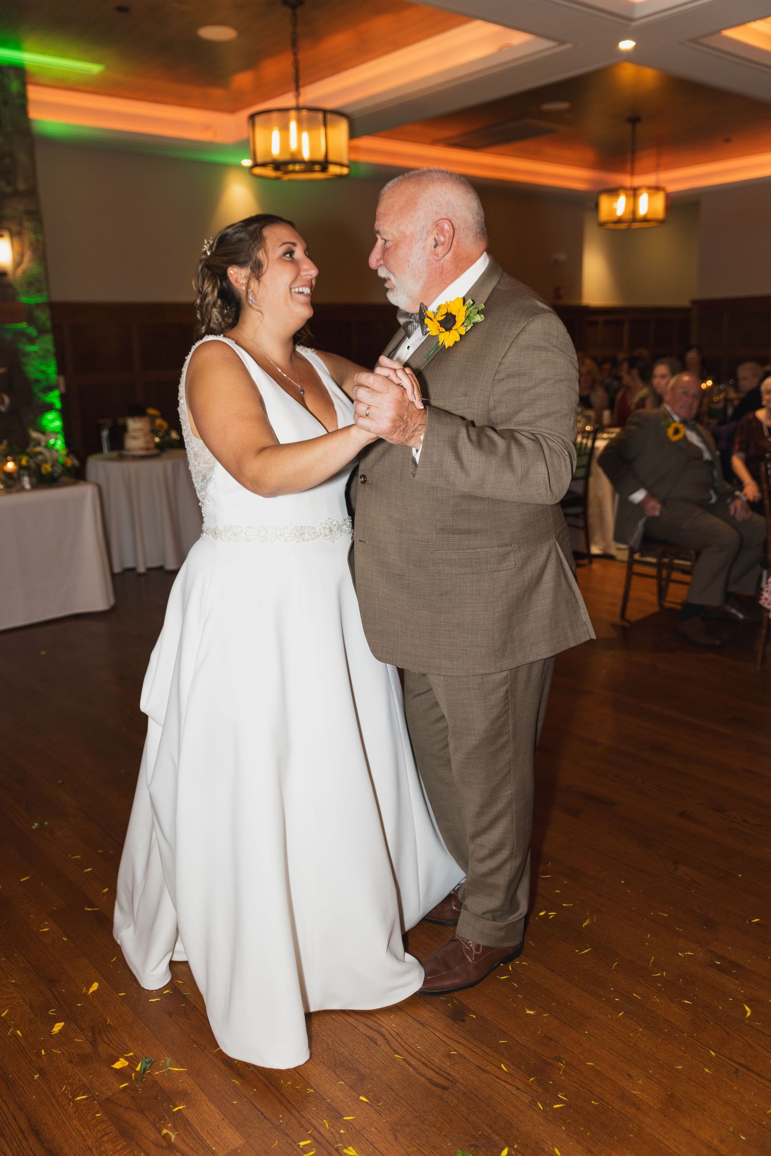 A couple shares a dance on a wooden floor during their wedding reception.