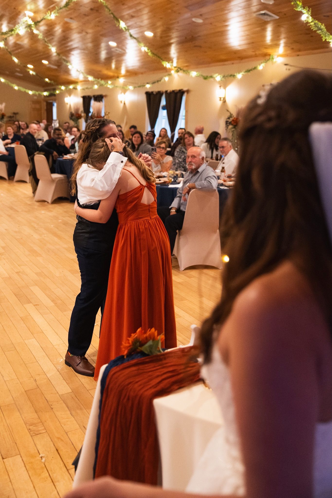 Wedding reception dance floor with couples dancing under warm string lights in a wooden hall.