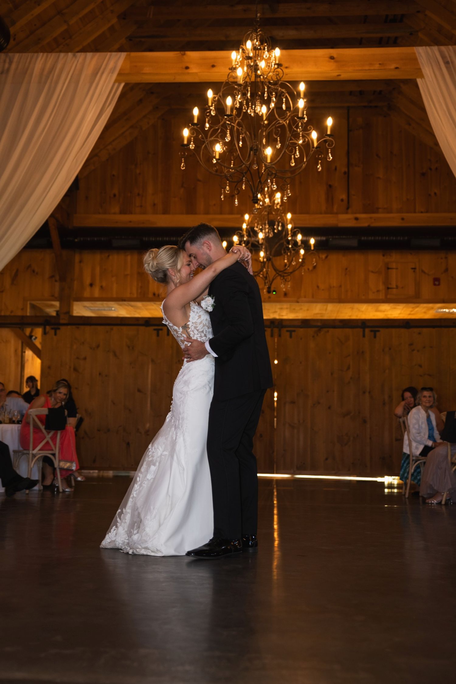 Wedding first dance sequence under rustic wooden beams and crystal chandeliers.