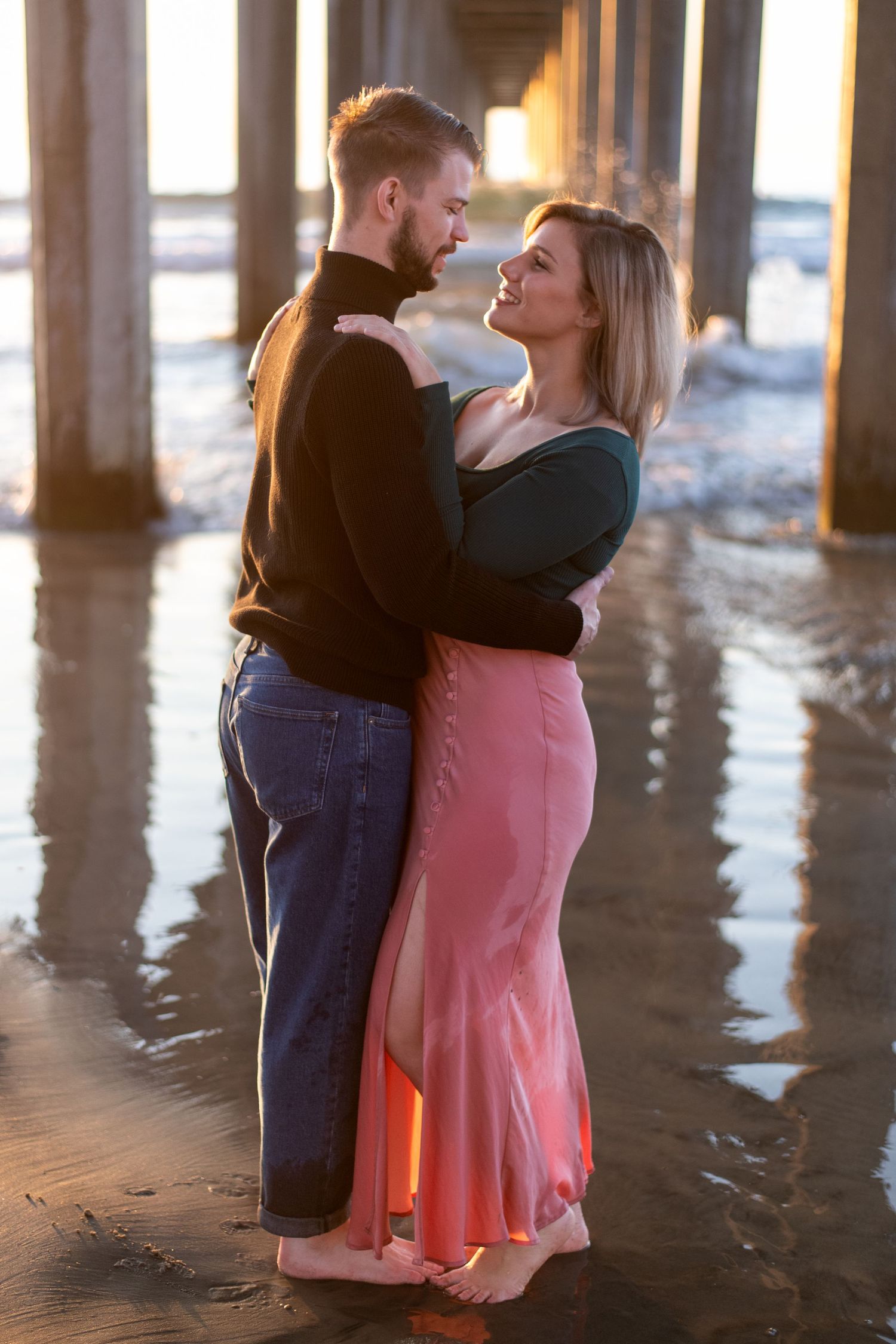 Family sharing tender moment under pier at beach during golden hour.