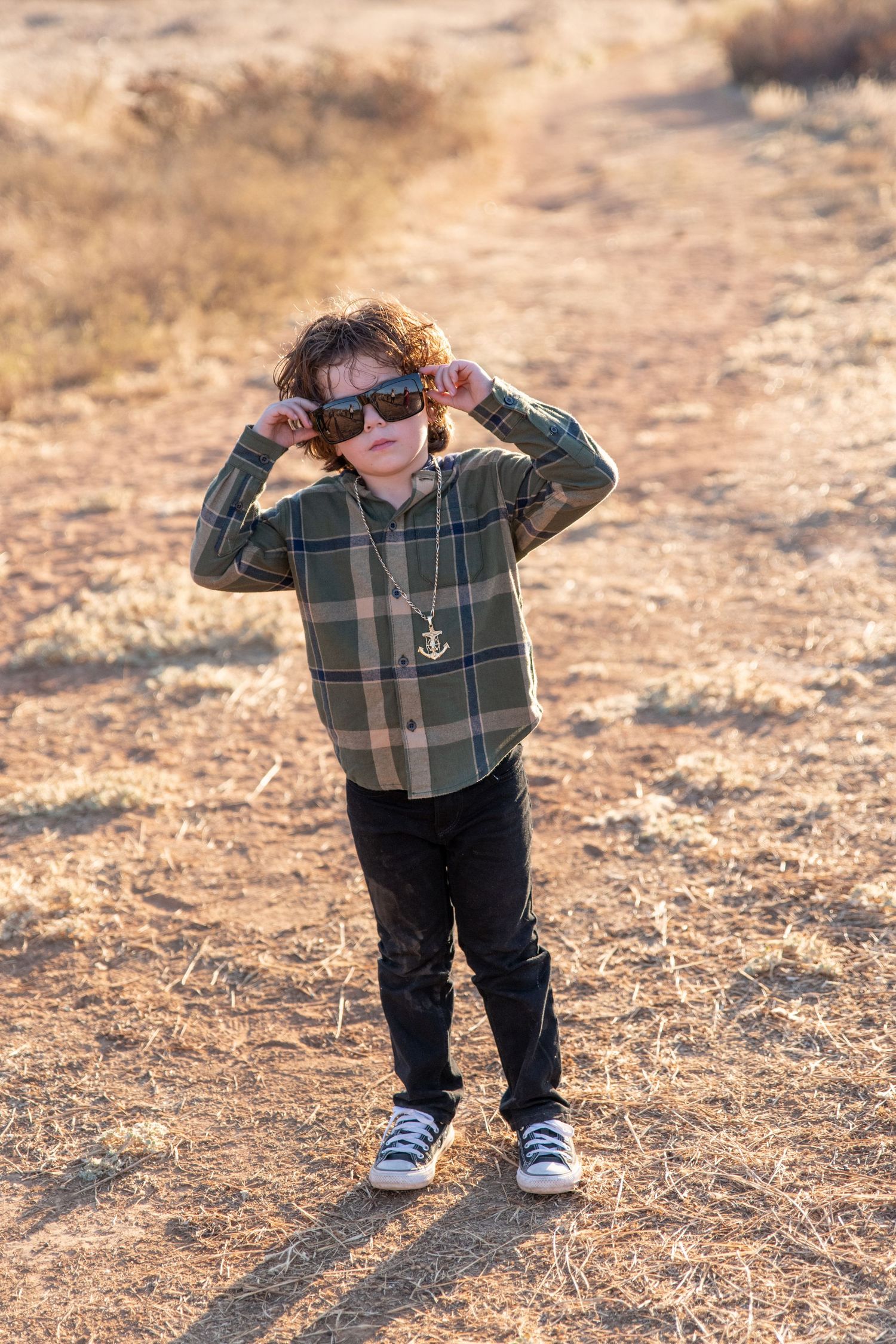 Child in plaid shirt and dark pants playing outdoors on dirt path.