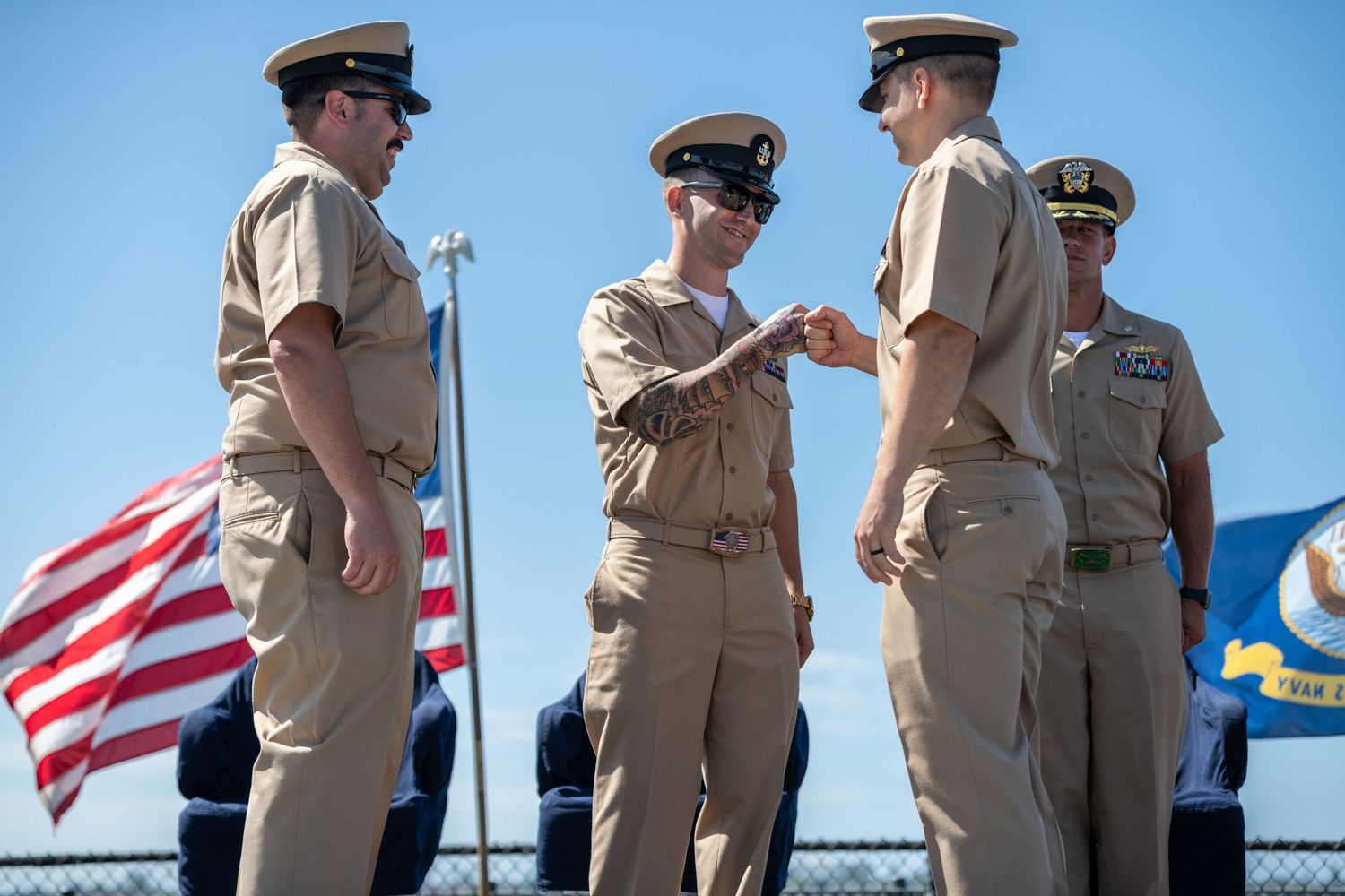 Naval officers in dress uniforms conduct a ceremony with American flag displayed.
